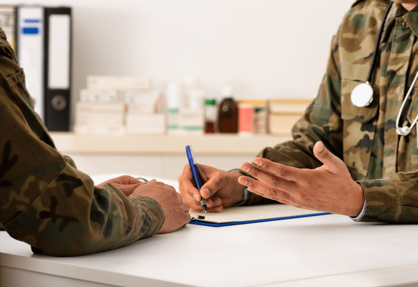 a man in camouflage with a stethoscope around his neck speaking to another man in camouflage