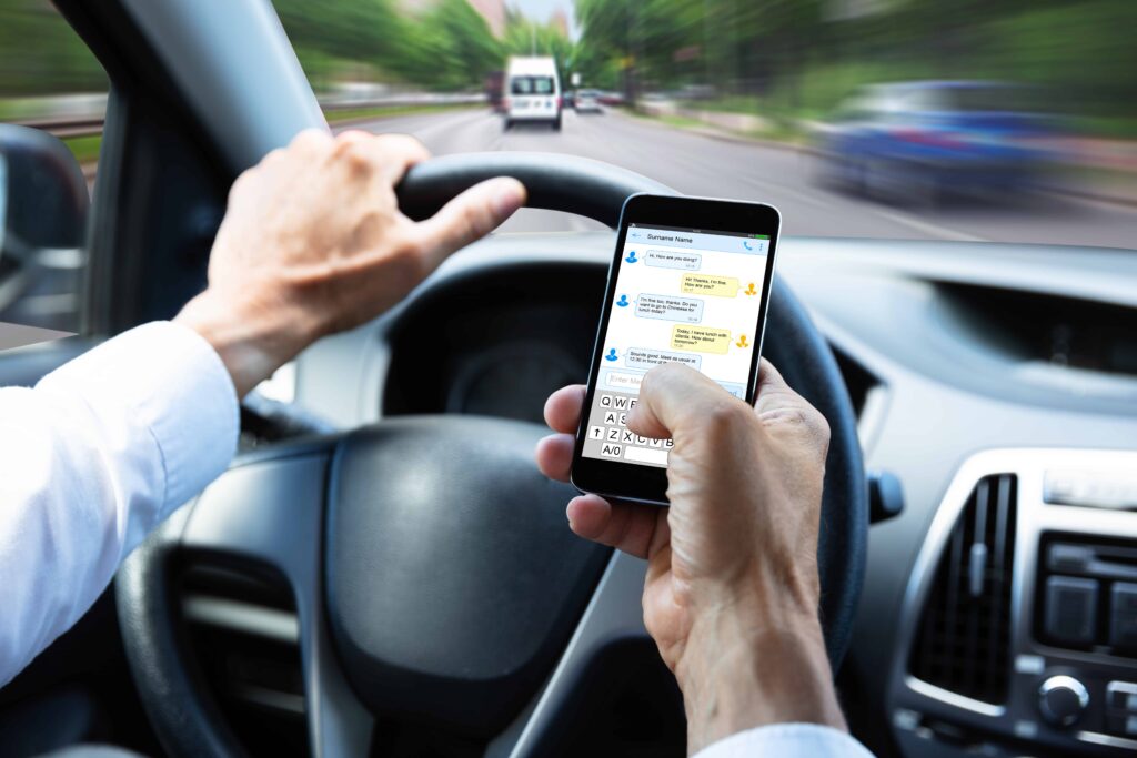 Driver texting on a smartphone while driving, highlighting dangerous distracted driving behavior.