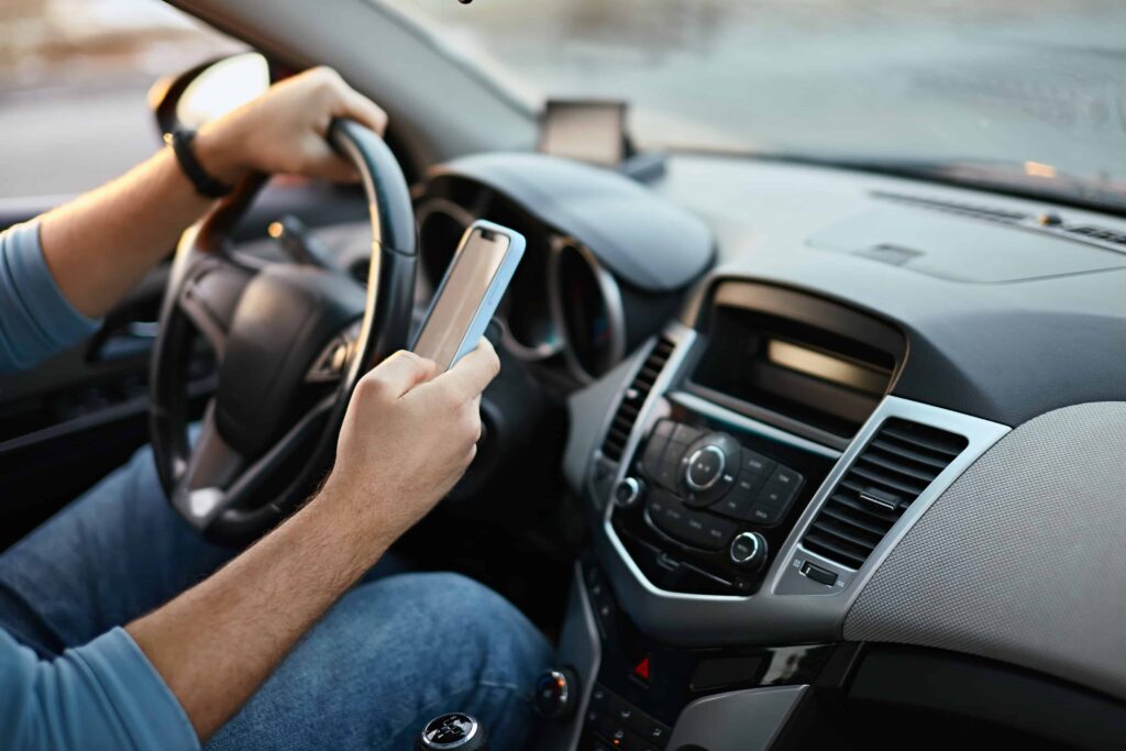 Driver texting on a smartphone while driving, showing dangerous distracted driving behavior.