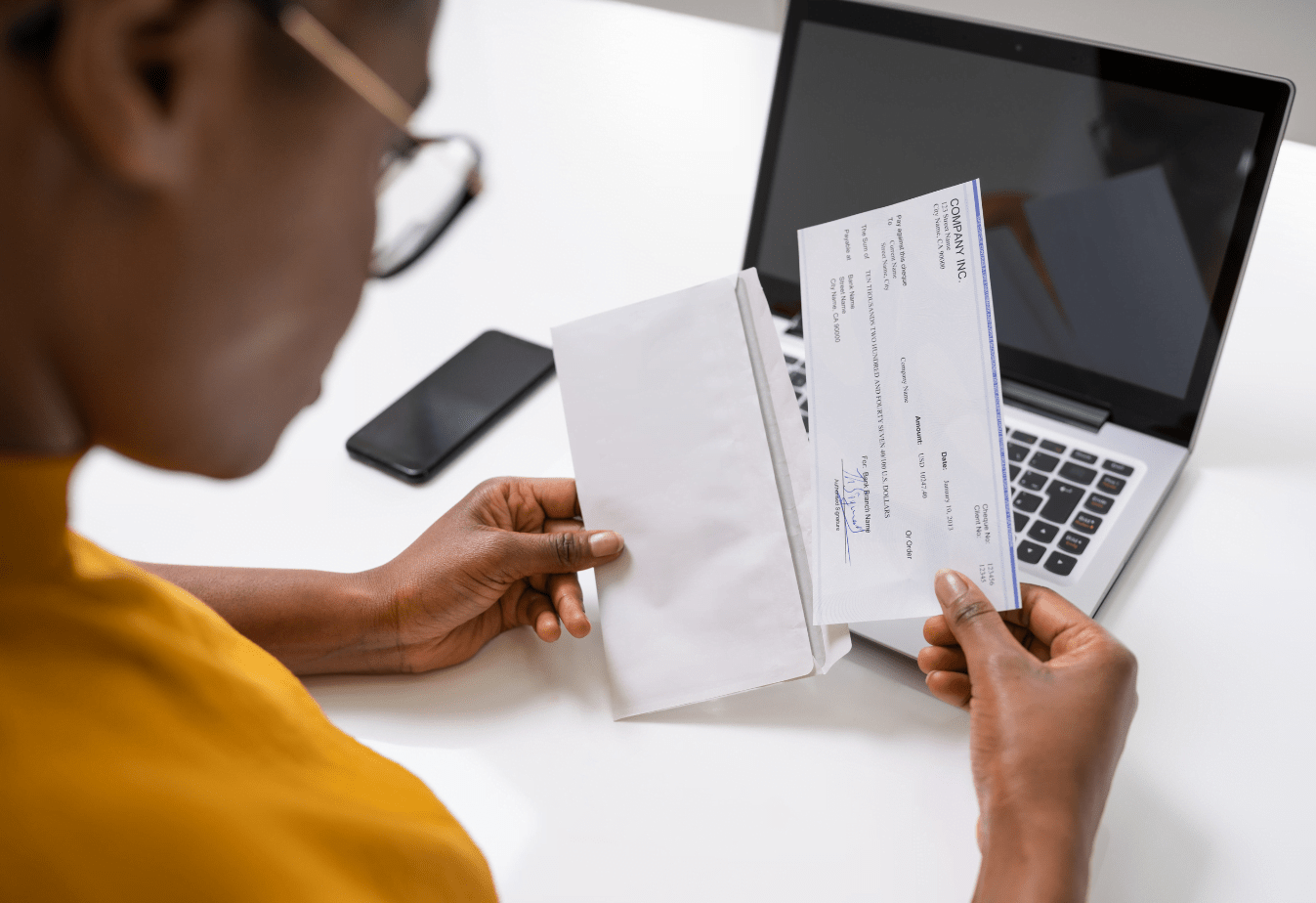 a woman holding an envelope and paycheck above a laptop keyboard