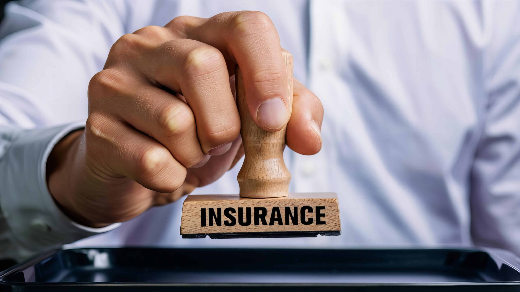 Close-up of a hand stamping an insurance approval document with a wooden insurance stamp.