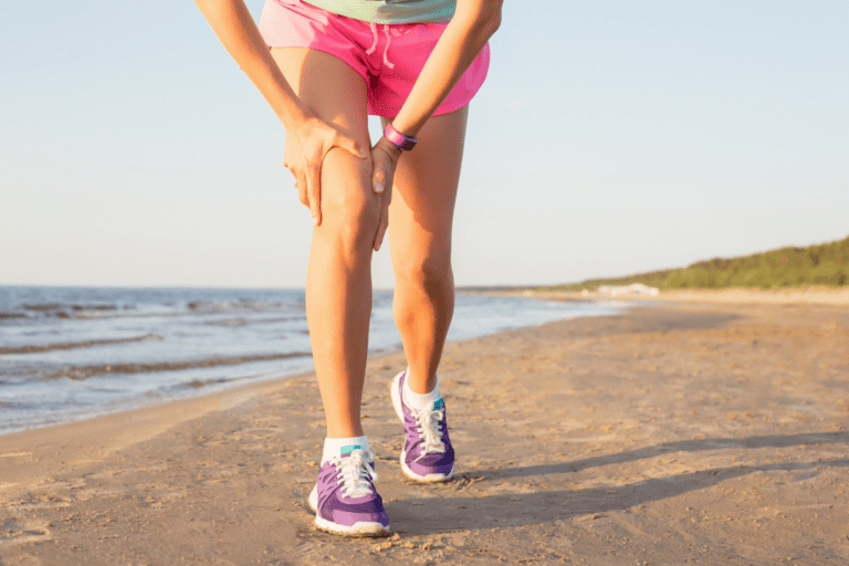 woman in running clothes on the beach with pain in her knee
