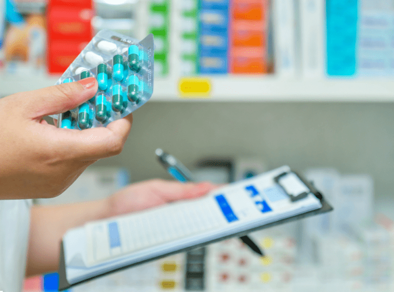 person's hand holding pills and a clipboard.