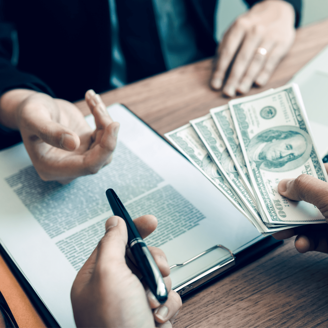 a woman about to sign a document while someone hands her a pen with one hand, and money in the other hand