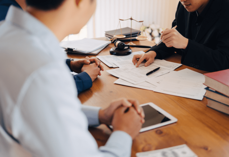 two people sitting on one side of a table listening to another person on the other side of the table pointing to papers