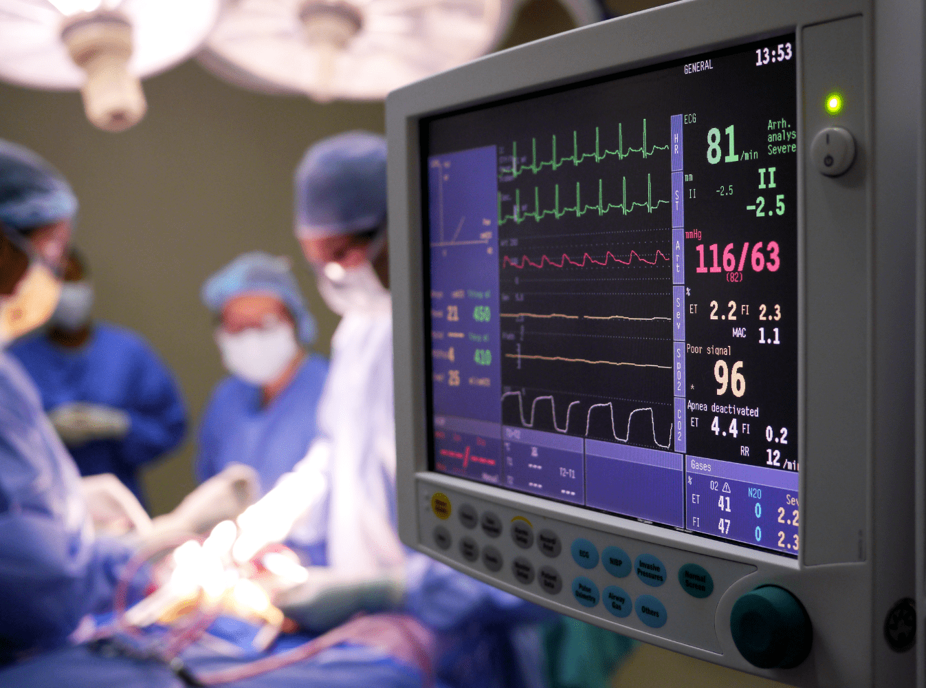 heart monitoring machine in the foreground, surgeons in the background