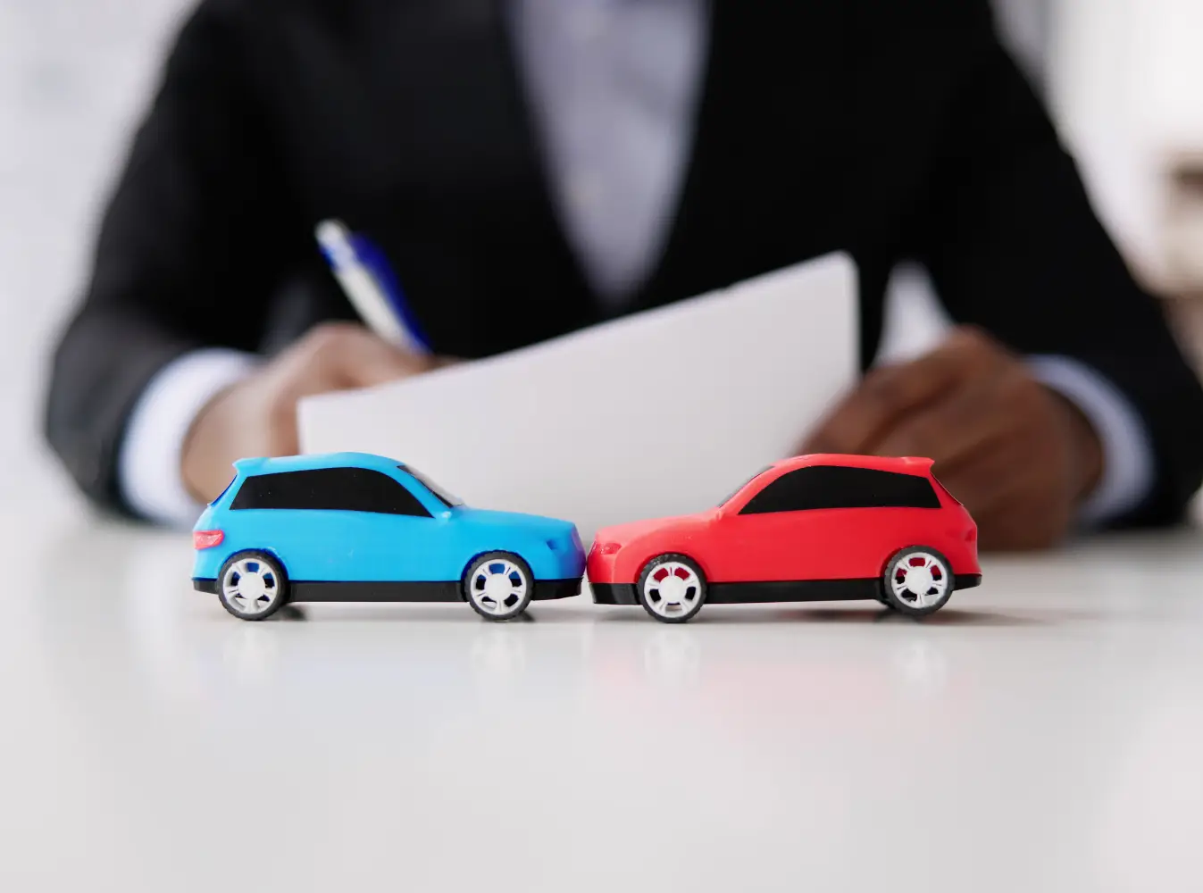 two toy cars facing each other in front of a person with pen and paper
