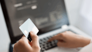 person holding a credit card in the foreground typing on a laptop in the background