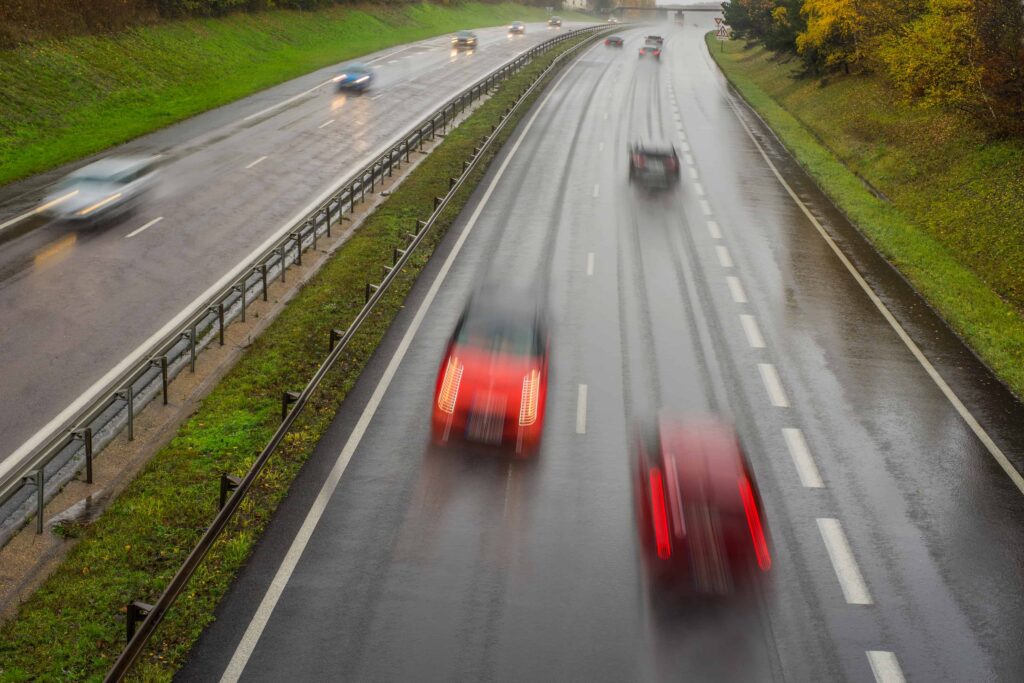 Cars driving on a wet highway in rainy weather with blurred motion showing slippery road conditions.