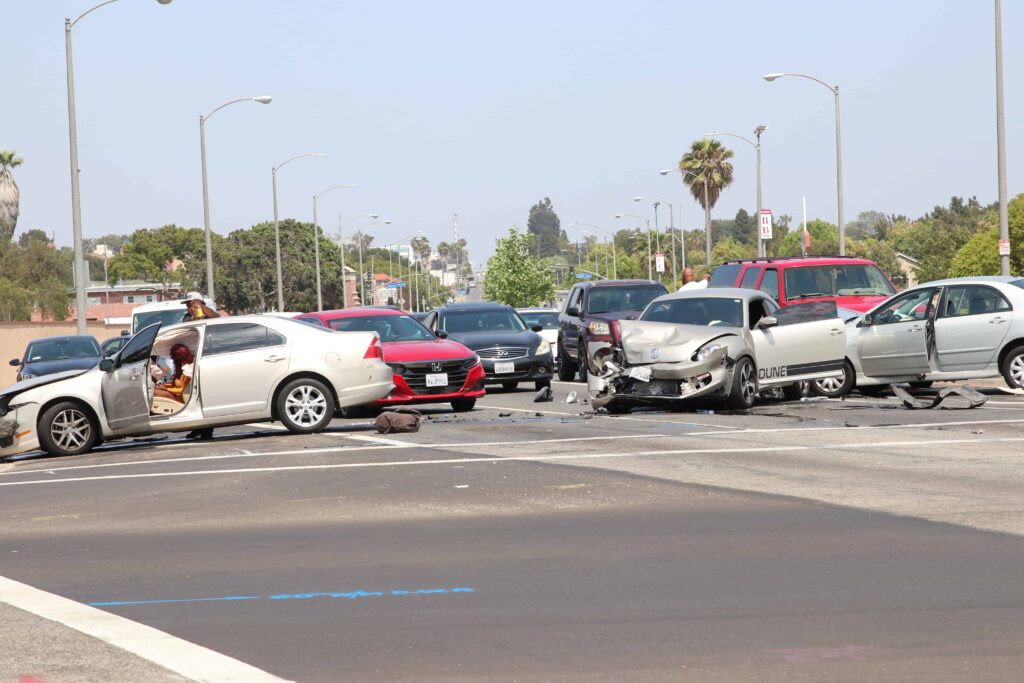 Multiple-car collision at a busy intersection with severe vehicle damage and open car doors.