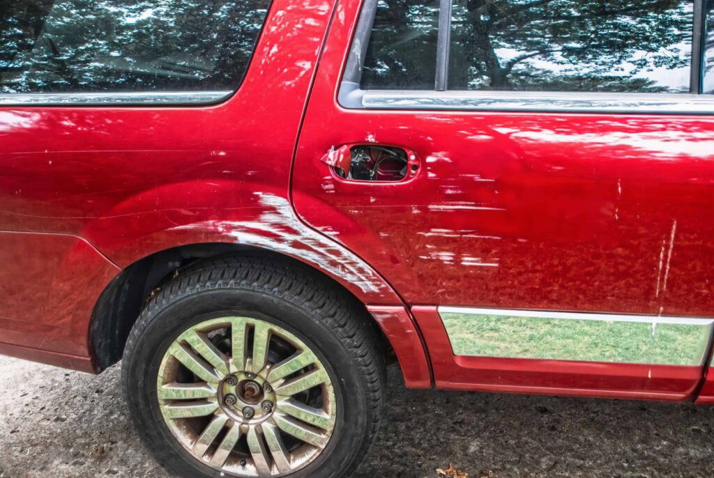 Close-up of red SUV with severe side scratches and missing fuel cap after minor collision damage.