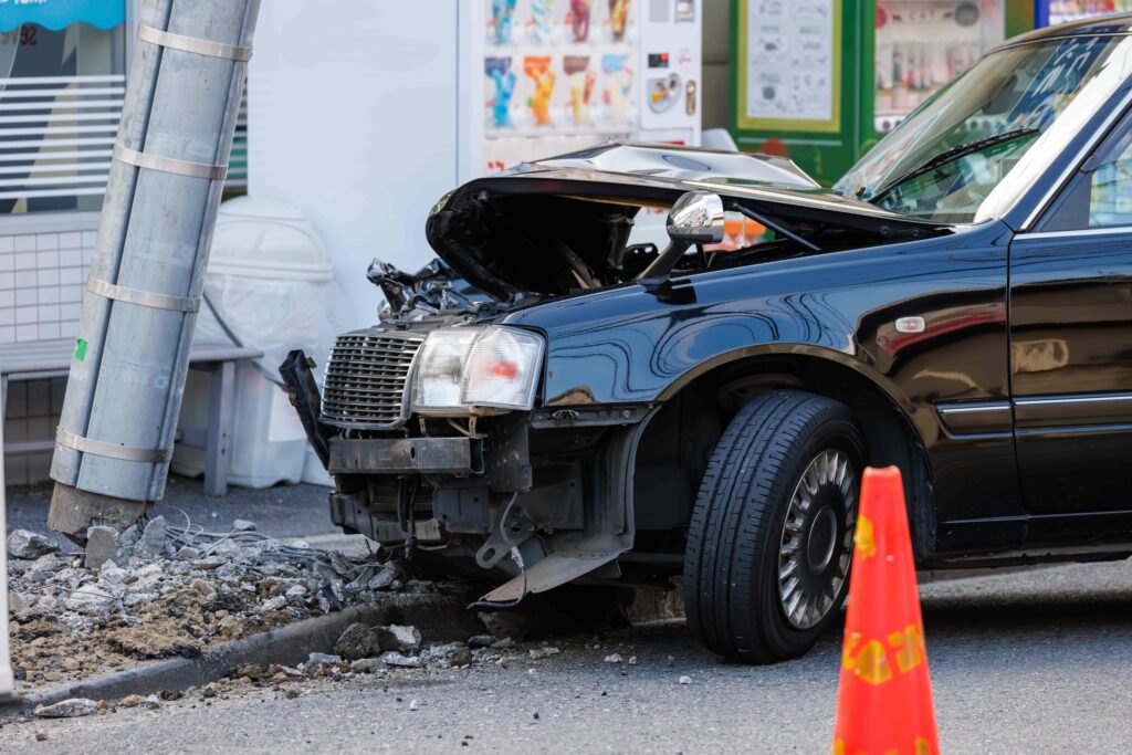 Black car crashed into a utility pole with severe front-end damage on a city street.