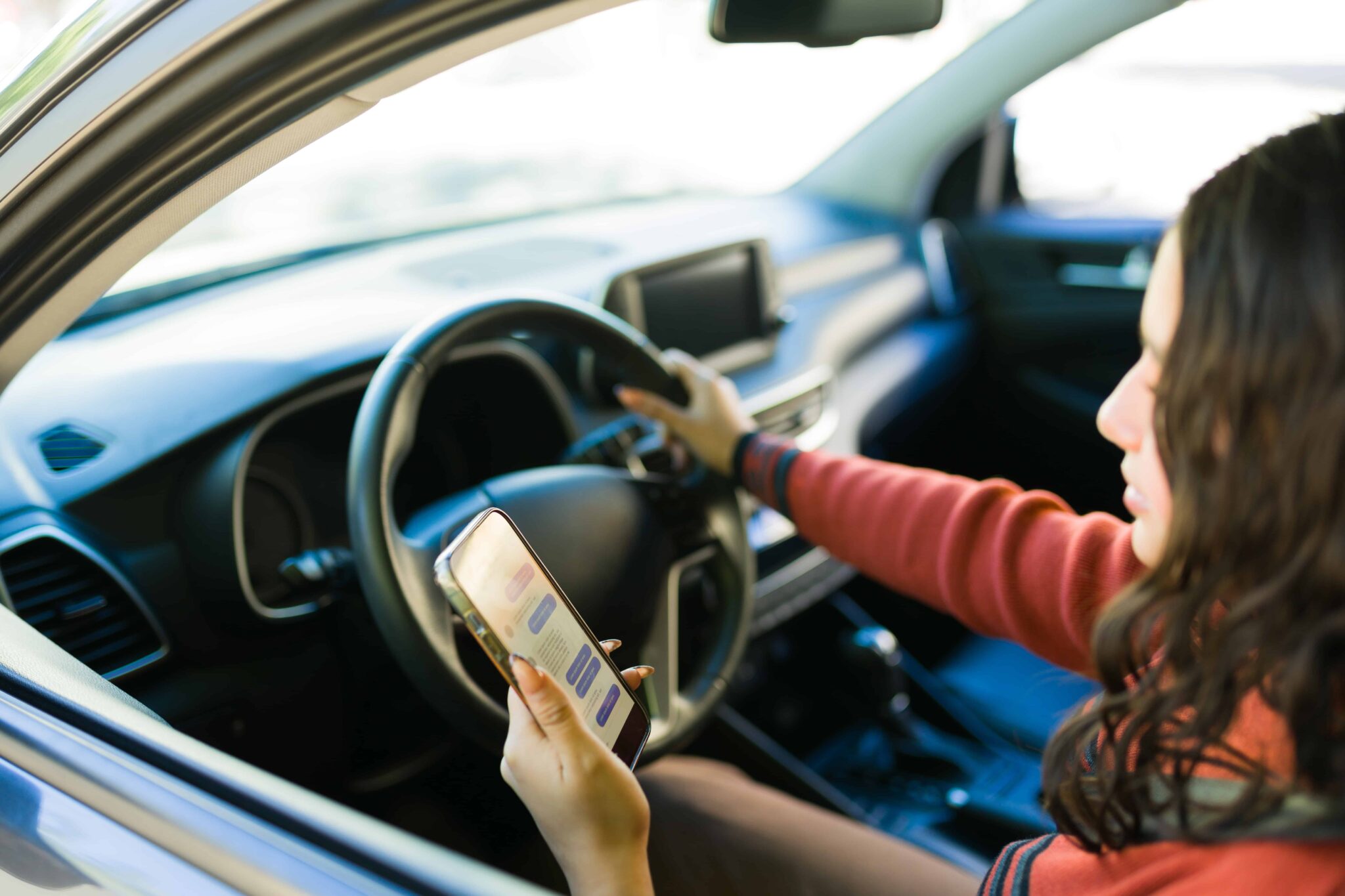 Driver using a phone while operating a car, illustrating distracted driving risk.