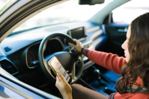 Driver using a phone while operating a car, illustrating distracted driving risk.