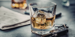 glass with dark alcohol next to car keys